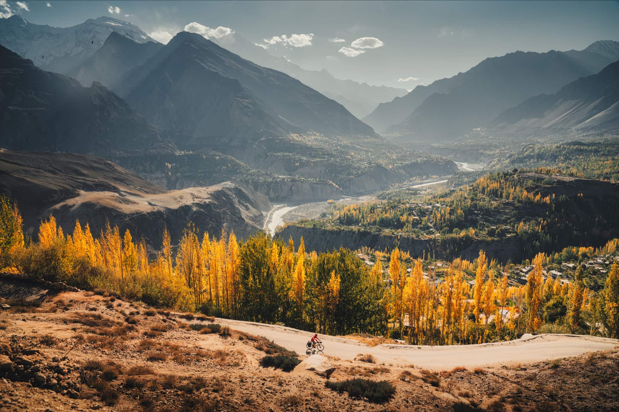 Landscape with mountains and trees with yellow leaves and in the distance Kamran Ali riding a belt driven bike