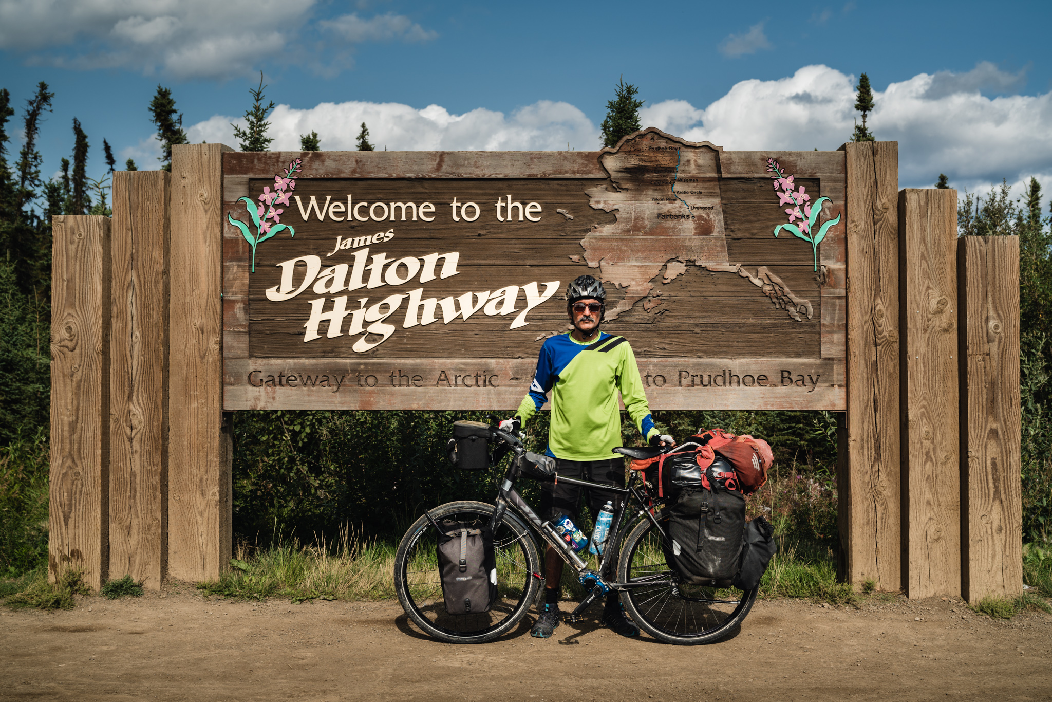 Kamran Ali  posing for a photo on the welcome sign to the James Dalton Highway